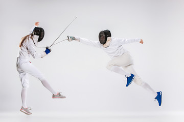 The men and woman wearing fencing suit practicing with sword against gray