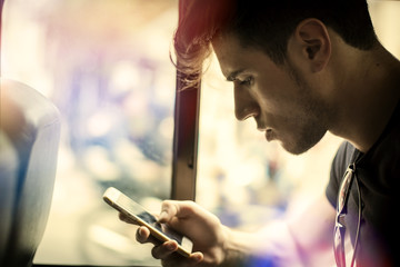 Young handsome man riding bus or pullman texting messages or using cell phone