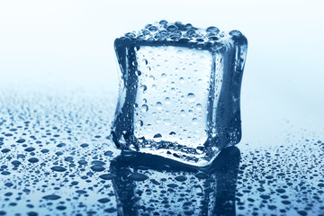 Transparent ice cube with reflection on blue glass with water drops