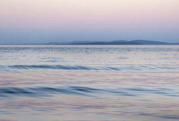 Waves with mountains lake landscape at dawn or dusk pink and blue background
