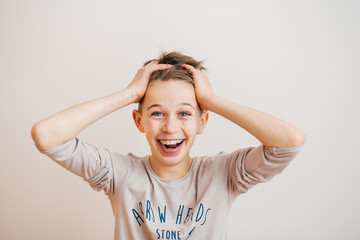 Portrait of a surprised  teenage boy holding his head on a light background