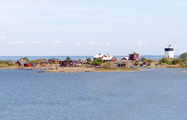 Lighthouse and some small red cottages on a tiny island in the s