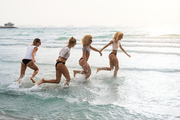 Four happy girlfriends running in water holding hands and laughing.