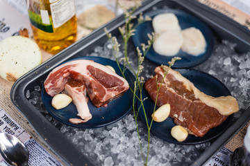 Beef, Pork, and Scallop Preparing for Cooking on Iced Plate with Olive Oil, Wine, Half of Onion and Black Pepper on Newspaper.
