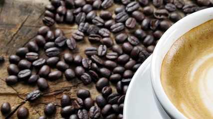 Cappuccino Coffee. A cup of latte, cappuccino or espresso coffee with milk put on a wood table with dark roasting coffee beans. Drawing the foam milk on top.
