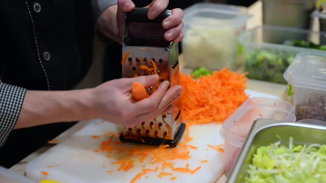 Chef rubs carrots on grater/Chef rubs carrots on metal grater in kitchen of restaurant