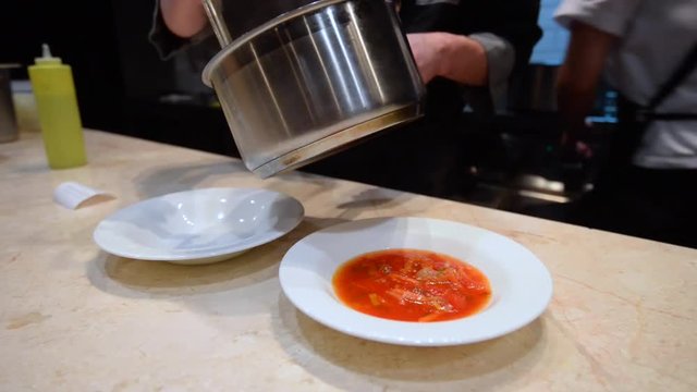 Chef pours red soup/Chef in black uniform pour red soup in a white dish on restaurant kitchen