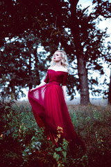 Fashion gorgeous young blonde woman in beautiful red dress in a fairy-tale forest. magic atmosphere. Retouched toning shot