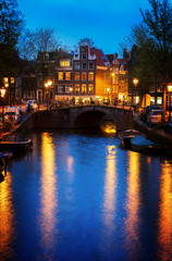 Naklejka premium Houses and bridge over canal with glowing lights at night, Amsterdam, Netherlands, retro toned