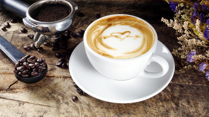 Cappuccino Coffee. A cup of latte, cappuccino or espresso coffee with milk put on a wood table with dark roasting coffee beans. Drawing the foam milk on top.