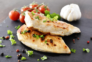 Grilled chicken breast on a slate plate with herbs and cherry tomatoes, garlic and peppercorns....