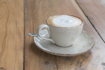White cup of coffee on wooden table in the coffee shop.