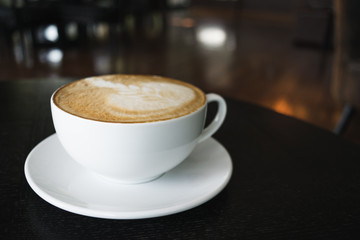 White cup of coffee on wooden table in the coffee shop.