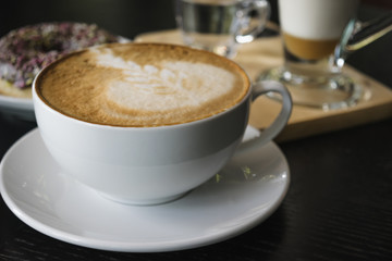 White cup of coffee on wooden table in the coffee shop.