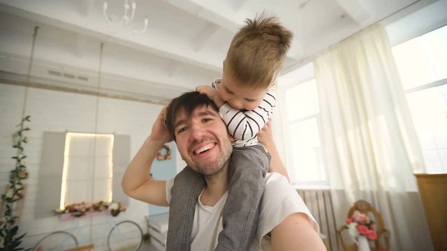 Happy father carrying his smiling son on neck and making selfie on video in bedroom