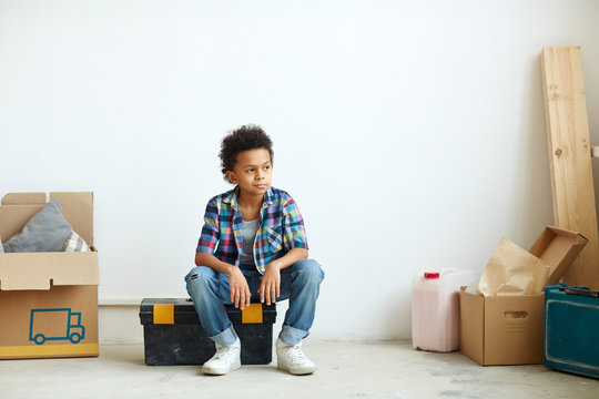 Little boy sitting on tool-box in his new room