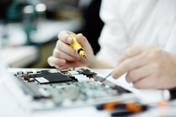 Fototapeta premium Closeup shot of unrecognizable man assembling circuit board using screwdriver and different tools on table in workshop