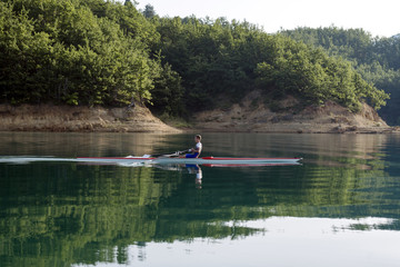 Fototapeta na wymiar A Young single scull rowing competitor paddles on the tranquil lake