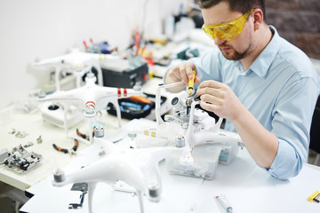 Portrait of modern man setting up new high tech drones and attaching cameras in electronic workshop