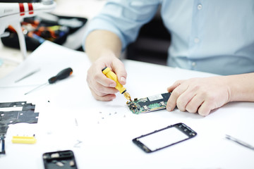 Closeup shot of male hands assembling smartphone on white table in workshop using screwdriver and other tools