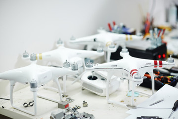 Several white high tech quadrocopter drones standing on workshop table in electronics lab