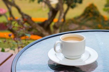 White ceramic cup of coffee on glass table in backyard. It is a drink for refreshment.