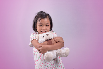 A girl hugging a teddy bear on a pink background.