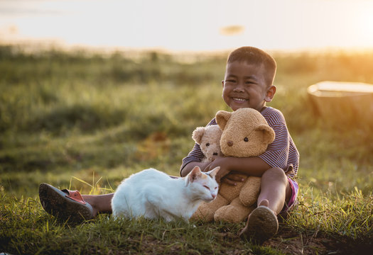 Boy hugging a teddy bear and a cat sitting in the garden.