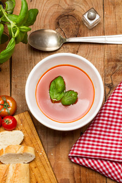 Sopa crema de tomate en cuenco blanco con albahaca sobre mesa de madera. Vista superior