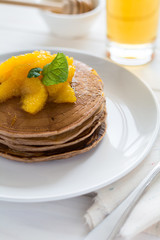 Traditional breakfast: stack of pancakes with orange slices and sweet sauce on white wooden table. Selective focus
