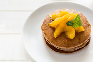 Traditional breakfast: stack of pancakes with orange slices and sweet sauce on white wooden table. Selective focus