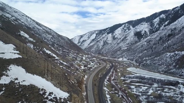 Aerial mountain canyon highway traffic descent. Wasatch Mountain Range central Utah. Highway in deep canyon valley traffic travel. Winter snow. Landscape scenic and rugged. Drone aerial flight.