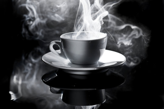 small white cup of steaming coffee on a black background