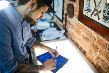 Worker of tattoo-salon drawing picture of adornment