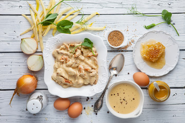 Chicken fillets in mustard and honey sauce, with ingredients on white wooden table