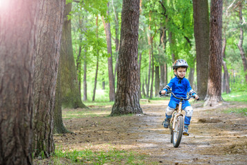 Obraz premium Happy cute blond kid boy having fun his first bike on sunny summer day, outdoors. child making sports. Active leisure for children. wear safety helmet. is smiling and cicling