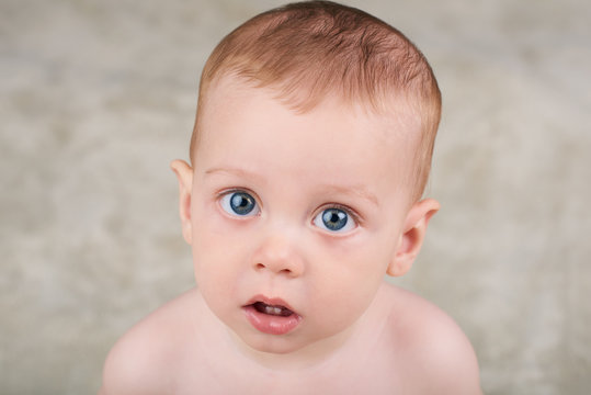 Cute white baby boy with large blue eyes looking up at camera with his mouth open as if intrigued by the camera.
