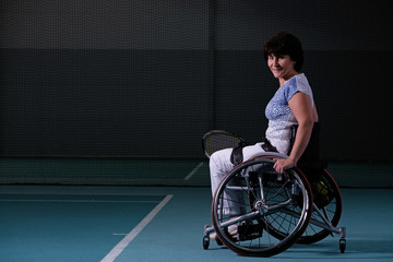 Fototapeta na wymiar Disabled mature woman on wheelchair playing tennis on tennis court.
