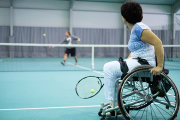 Disabled mature woman on wheelchair playing tennis on tennis court.
