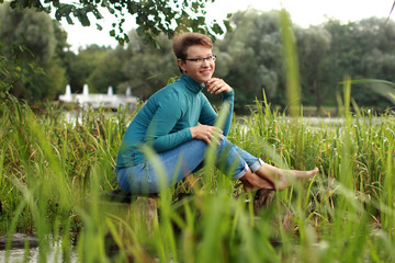 Naklejka na ściany i meble Beautiful emotional girl sits on a lake among the grass and wate
