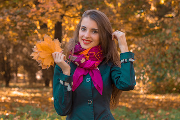 Naklejka na ściany i meble beautiful smiling girl in a pink scarf stands in the Park and keeps the leaves