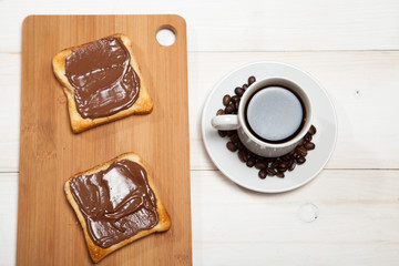 cup of coffee and toast with chocolate on a white wooden table