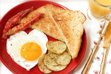 Breakfast in bed with egg heart Bacon bread toast roasted potatoes and orange juice served in wooden tray for Valentine's day