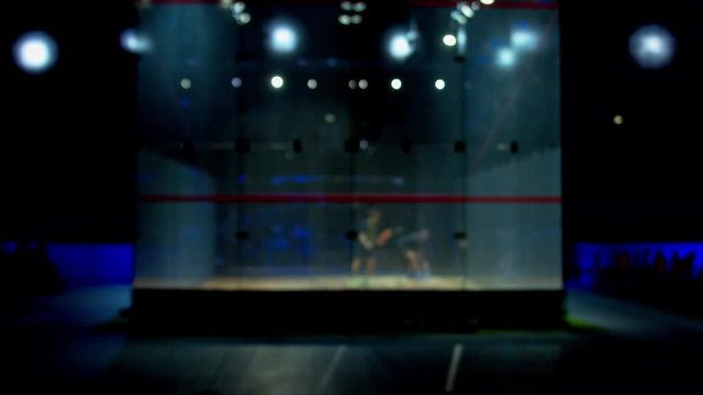 DEFOCUSED BACKGROUND Two people playing squash in a glass court inside a large venue. 4K UHD RAW edited footage
