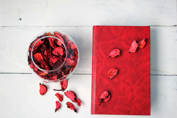 Красная книга на белом столе и прозрачная стеклянная ваза с лепестками цветов