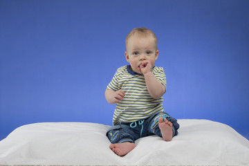 Fototapeta premium Adorable little baby boy, sitting on the white blanket, studio shot, isolated on blue background