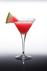 Cocktail with raspberry vodka, grenadine syrup and watermelon slice, on black gradient reflective background.