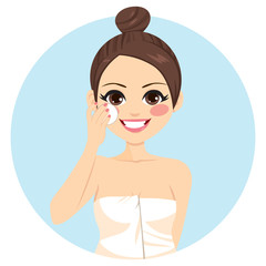Cute brunette woman with hair bun cleaning face with white cotton pad