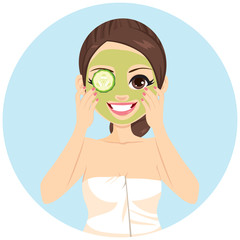 Beautiful brunette woman with applying cucumber slices on her green mud cleansing spa treatment