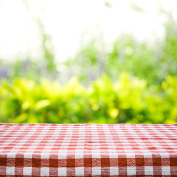 Red checkered tablecloth texture top view with abstract green from garden background.